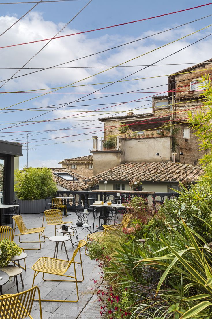 Una terrazza con sedie gialle circondata da un giardino verde, in un contesto urbano.