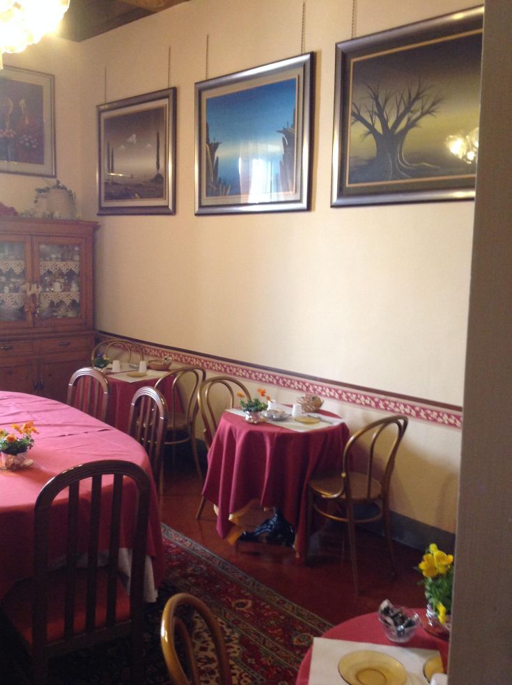 Ambiente interno di un ristorante con tavoli rotondi e decorazioni alle pareti. Atmosfera intima e conviviale.