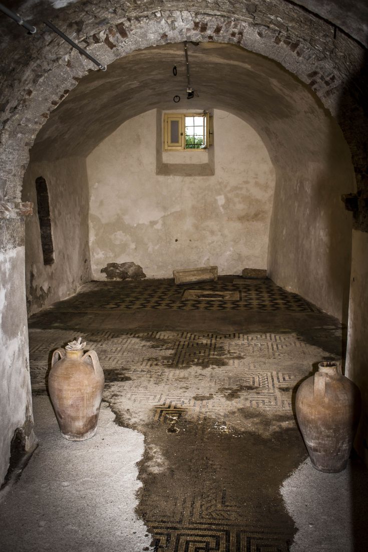 Interior of a historic building featuring terracotta vases and a mosaic-decorated floor.