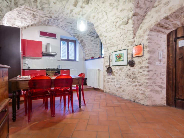 Cuisine moderne en pierre, agrémentée de détails colorés et éclairée par des spots suspendus.