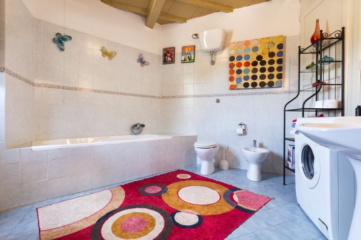 Salle de bain spacieuse avec baignoire, détails décoratifs vifs et lave-linge, située dans un cadre agréable.