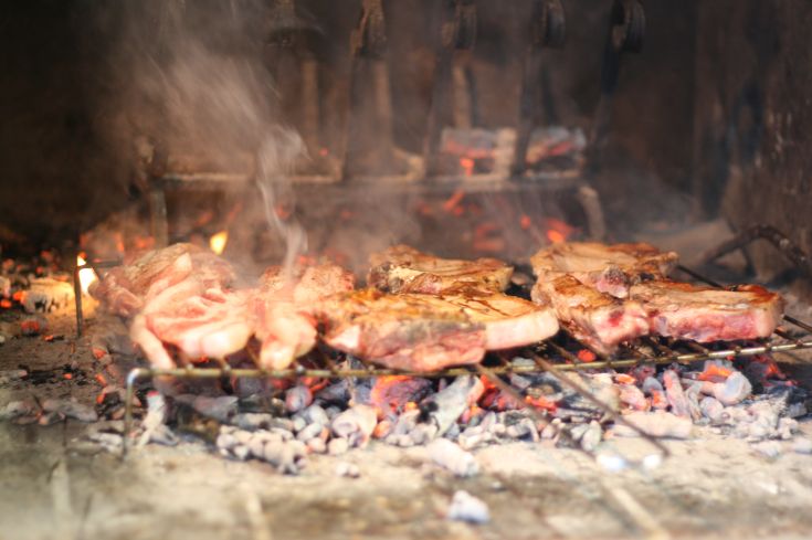 Gemischtes Grillfleisch, das über den Kohlen brutzelt, umgeben von einer Atmosphäre aus Rauch und Wärme.