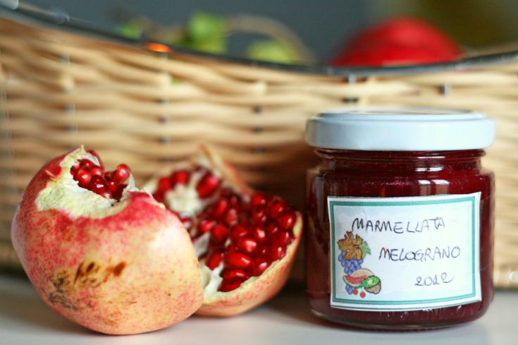 Ein Glas Granatapfelmarmelade neben einem halbierten Granatapfel.