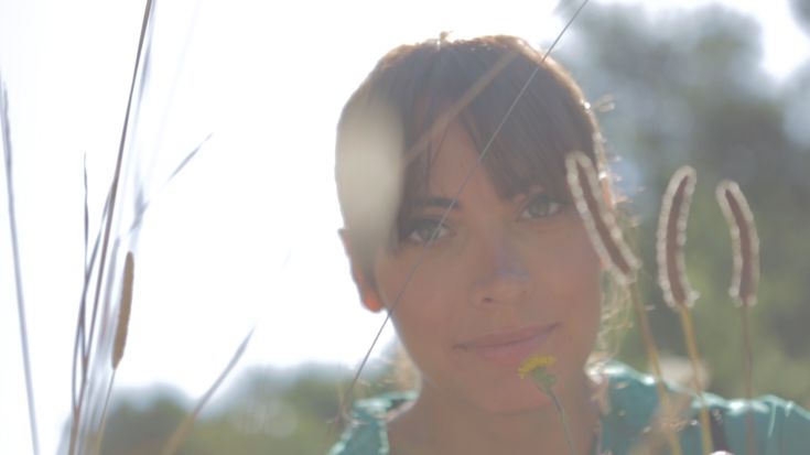 Porträt in einem Feld umgeben von Pflanzen und Blumen, das eine Atmosphäre der Ruhe vermittelt.