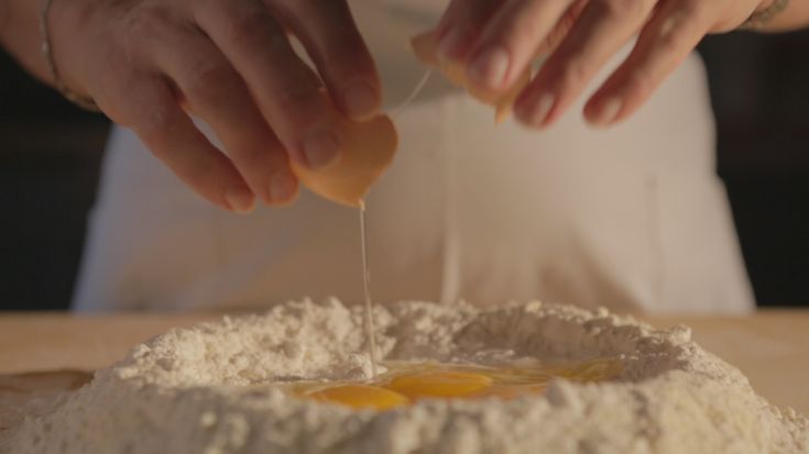 Ein Koch schlägt Eier auf eine Mehloberfläche, um frische Pasta zuzubereiten.