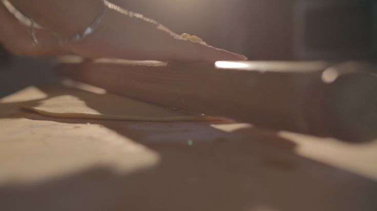 Eine Hand, die den Teig mit einem Nudelholz in einer ordentlichen und heimeligen Umgebung ausrollt.