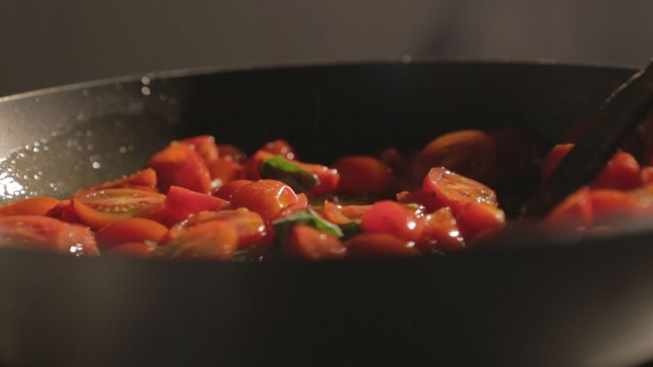 Frische Zutaten beim Kochen: Kirschtomaten und Basilikum. Ein einfaches und leckeres Gericht in der Pfanne zubereitet.
