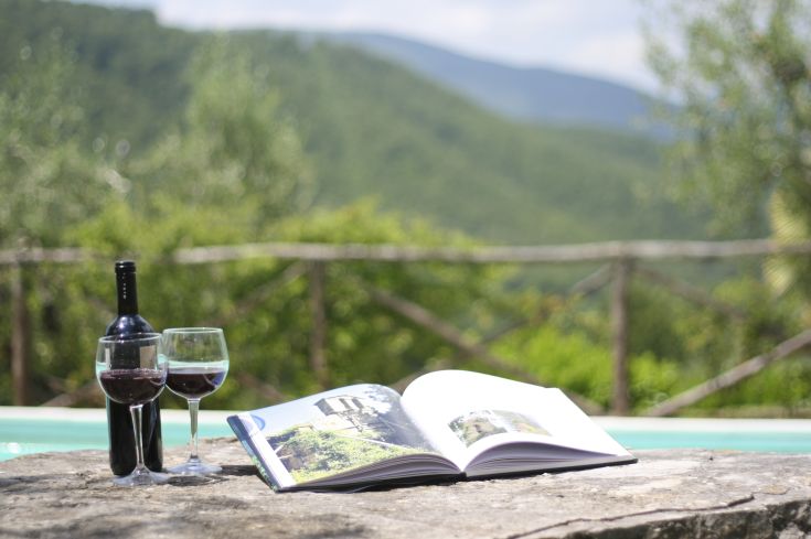Ein Tisch im Freien mit einer Flasche Wein und einem offenen Buch, umgeben von üppiger Natur.