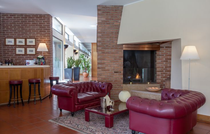A hotel lounge with red sofas and a contemporary fireplace. Bright space with simple furnishings.