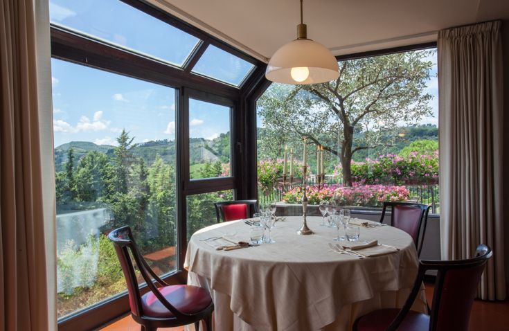 Cozy dining table inside a restaurant with a view of hills and flowers.