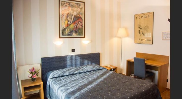 Camera semplice e confortevole con letto matrimoniale e scrivania, decorata con elementi d'arredo funzionali.