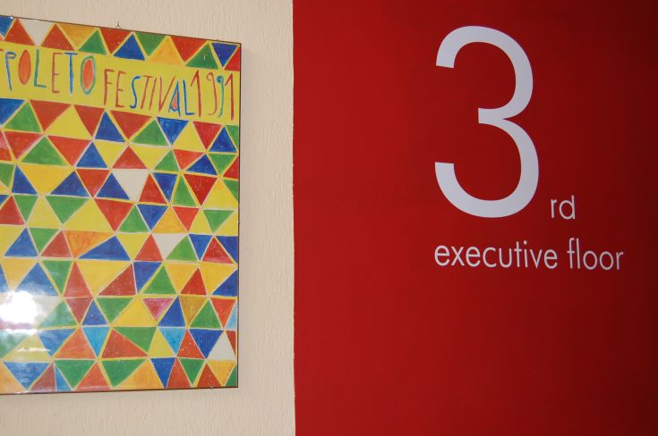 Signage indicating the third floor of a building, with a Spoleto Festival 1991 poster in the background.