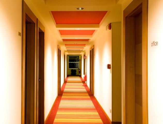 A well-lit corridor with doors to various rooms and striped carpeting.