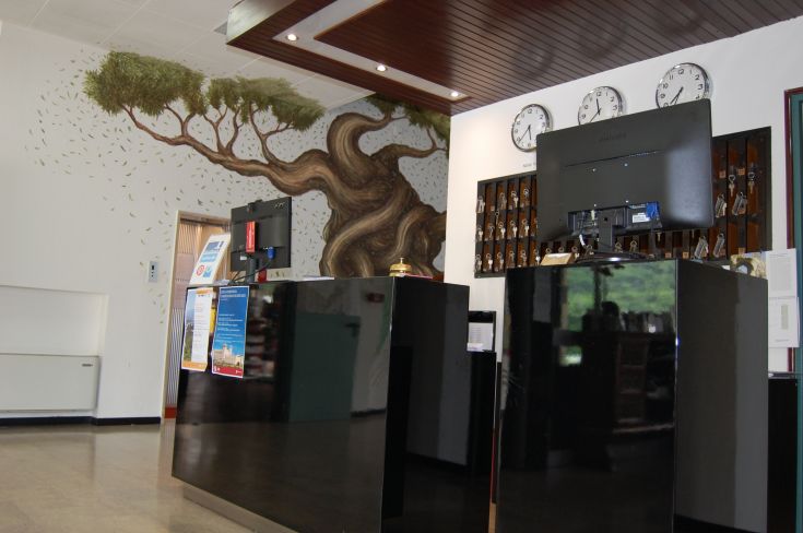 Hotel Arca reception featuring a mural of an olive tree and clocks hanging on the walls.