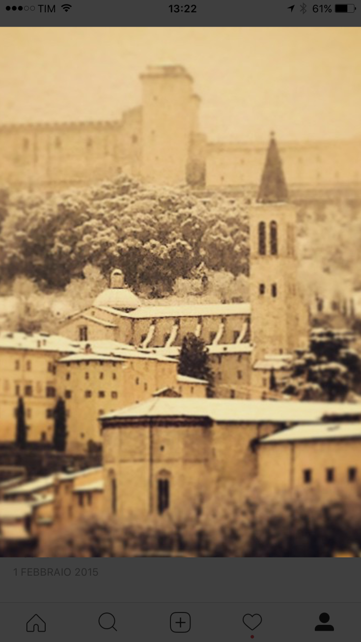 Winter scene of an ancient village, showcasing clearly visible buildings and a bell tower, surrounded by trees and greenery.