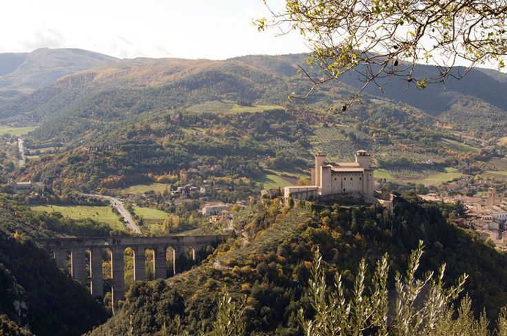 Eine Landschaft mit sanften grünen Hügeln, einem Gebäude und einem typischen Viadukt aus Umbrien.