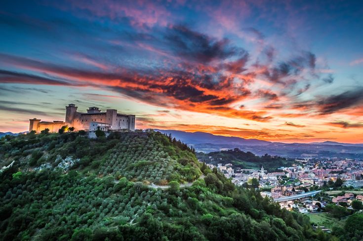 Eine Burg auf einem Hügel bei Sonnenuntergang, umgeben von Olivenhainen mit einem atemberaubenden Ausblick.