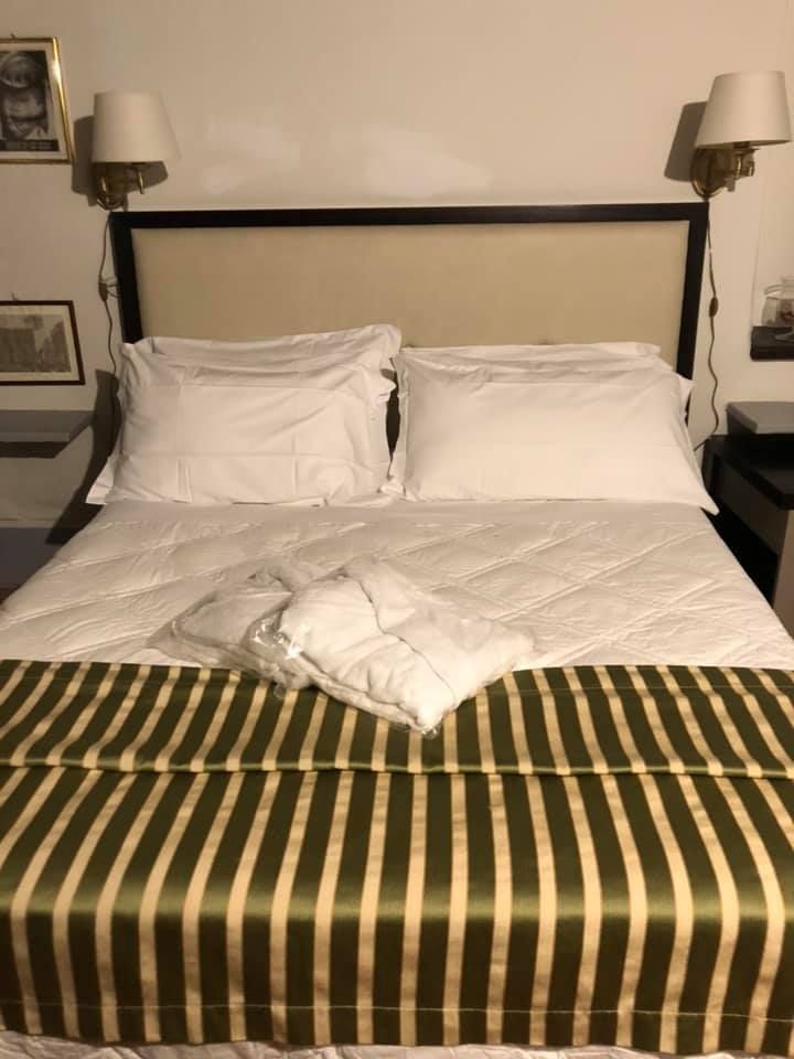 Una camera da letto semplice con un letto matrimoniale, lenzuola bianche e una coperta a righe verdi.