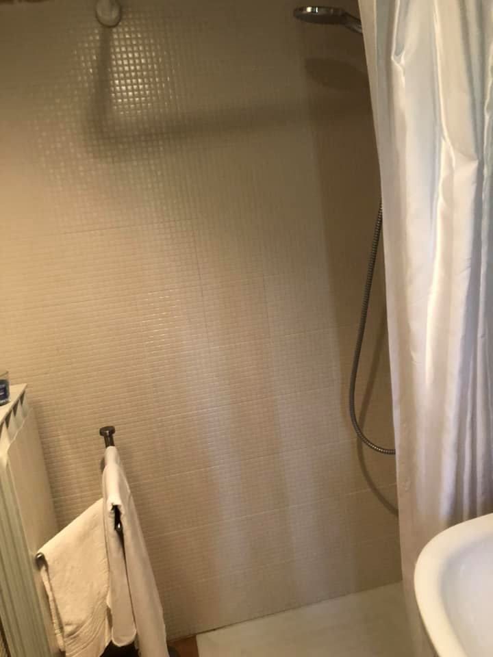 Doccia semplice e funzionale con tende e piastrelle chiare sui muri.