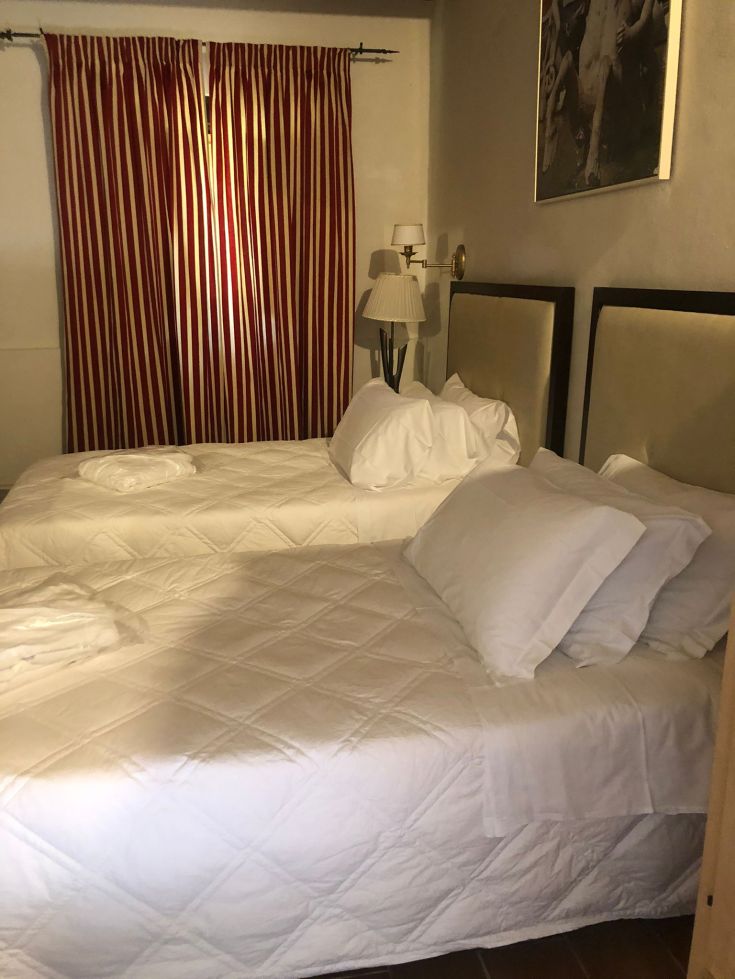 Camera con due letti singoli, arredamento essenziale e tende a righe rosse e bianche.