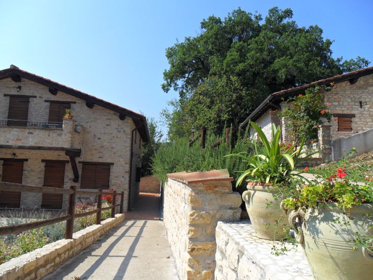 Zwei ländliche Gebäude in einem grünen Gebiet in Umbrien, umgeben von Pflanzen und Blumen.