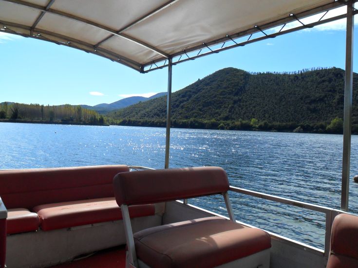 Eine friedliche Szene von einem Boot, mit üppigen Bergen, die einen ruhigen See umgeben.