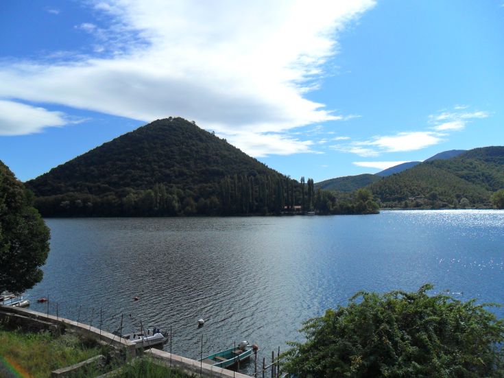 Ein ruhiger See, umgeben von grünen Hügeln und einem klaren Himmel, der eine friedliche Naturlandschaft darstellt.