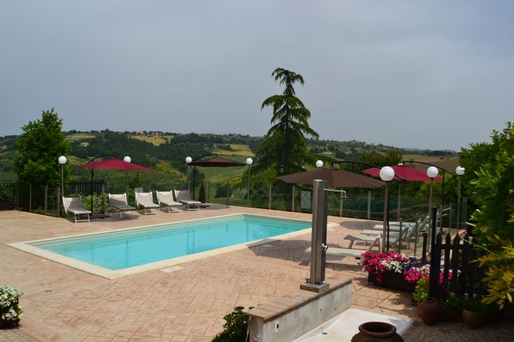 Una piscina immersa nella natura, circondata da alberi e vegetazione, con panorama sulla valle.