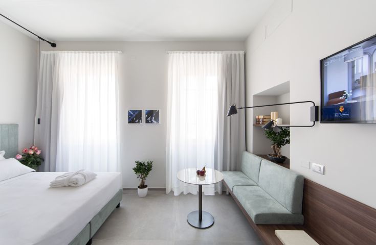 Une chambre d'hôtel simple et lumineuse avec un lit, un canapé, une télévision et un mobilier contemporain.