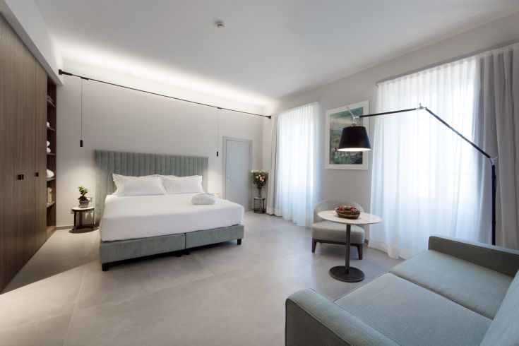 Chambre spacieuse et bien éclairée avec un lit double, un fauteuil confortable et une table simple pour une ambiance chaleureuse.