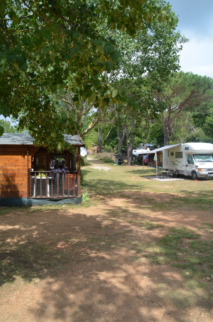 Un'area campeggio tranquilla circondata da alberi, con chalet e camper disposti ordinatamente.