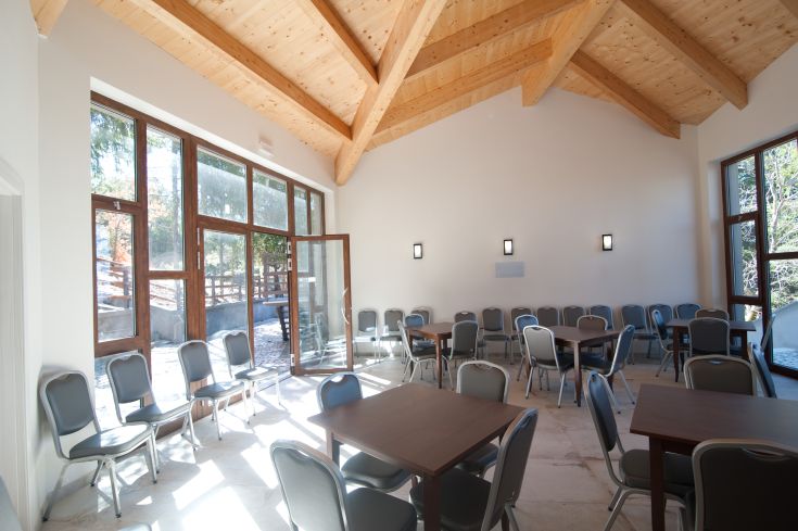 Environnement lumineux avec de grandes fenêtres et des poutres en bois apparentes, idéal pour des réunions et des événements.