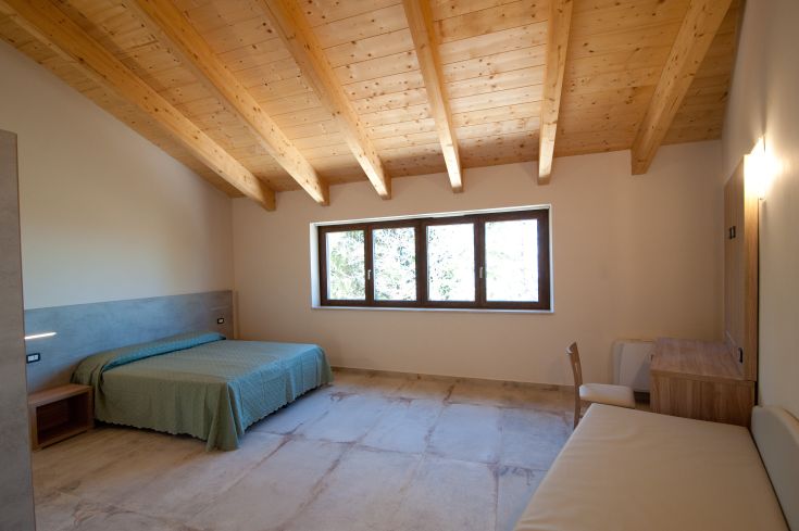 Chambre d'hôtel avec plafond en bois, lits confortables et grandes fenêtres offrant une vue paisible.