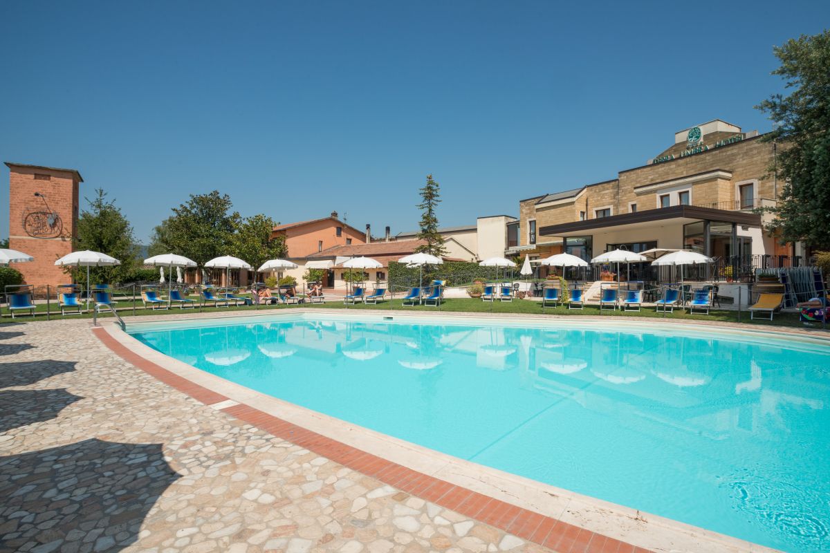 An outdoor pool with sunbeds and umbrellas, located in the garden of a hotel in Umbria.