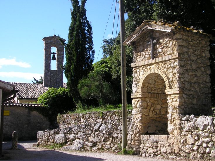 Un panorama del paesaggio di Monteluco con edifici storici in pietra e una chiesa con campanile.