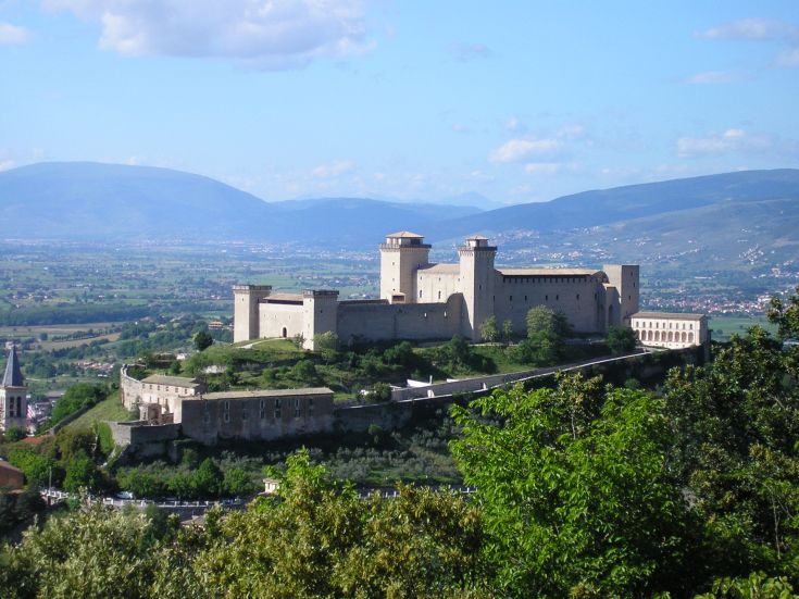 Castello situato in un paesaggio collinare caratterizzato da verdi colline e cielo sereno, rappresenta un'architettura storica.