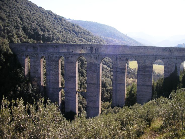 Un ponte si erge tra colline verdi, circondato da alberi e natura tranquilla.