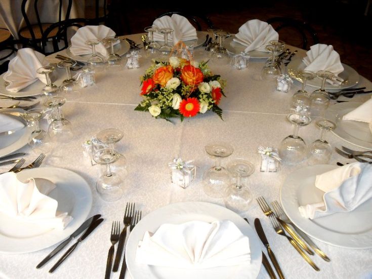 Un tavolo semplice allestito per un evento, con decorazioni floreali e stoviglie disposte ordinatamente.