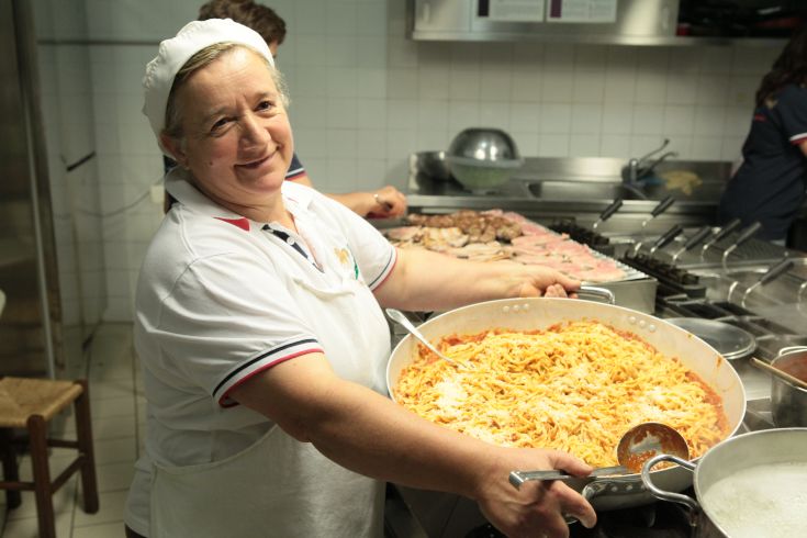 Una cuoca sorridente serve un piatto di pasta caldo in una cucina familiare.