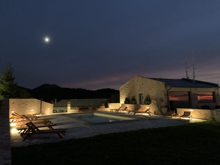 Panorama serale di un agriturismo con piscina, immerso nel verde delle montagne e illuminato dalla luce della luna.