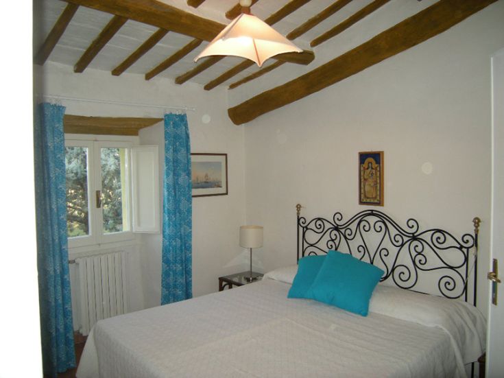 A simple bedroom with a double bed, adorned with blue curtains and wooden details.