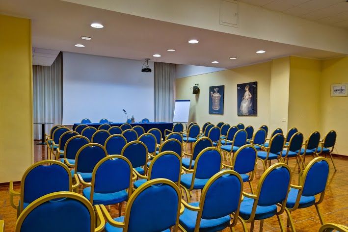 A conference room set up for meetings with blue chairs and a stage equipped with technology.