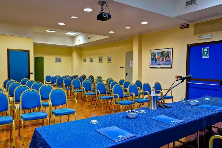 Conference space with blue chairs and a table, equipped with a projector and multimedia tools.