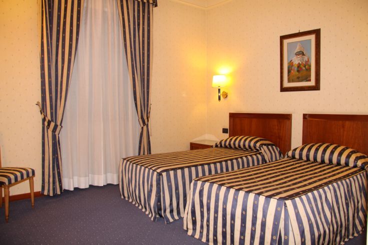 Camera semplice con letti singoli, tende a strisce e decorazioni sobrie. Adatta per un soggiorno tranquillo.