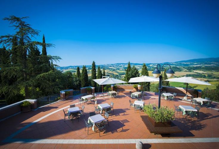 Terrazza con tavoli e ombrelloni immersa nel verde, ideale per momenti di relax.