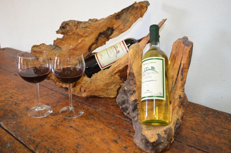 Due bicchieri di vino appoggiati su un tavolo in legno, circondati da varie bottiglie di vino. Ambiente informale e accogliente.