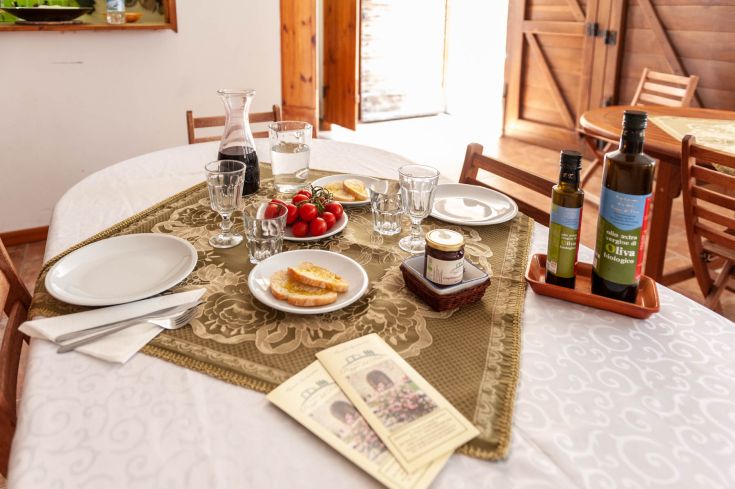 Un tavolo apparecchiato con pietanze, pomodorini, olio d'oliva e vino in un ambiente confortevole.