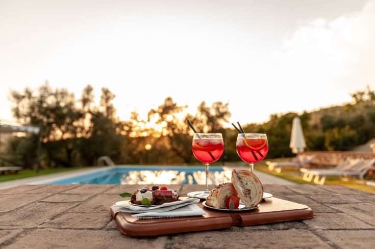Cocktail e dolci serviti a bordo piscina, illuminati dalla luce del tramonto. Un momento di relax e piacere.