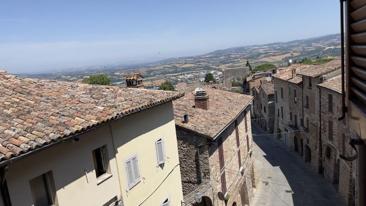 Eine Szene eines historischen Dorfes mit Kopfsteinpflasterstraßen und Gebäuden, umgeben von üppigen grünen Hügeln.