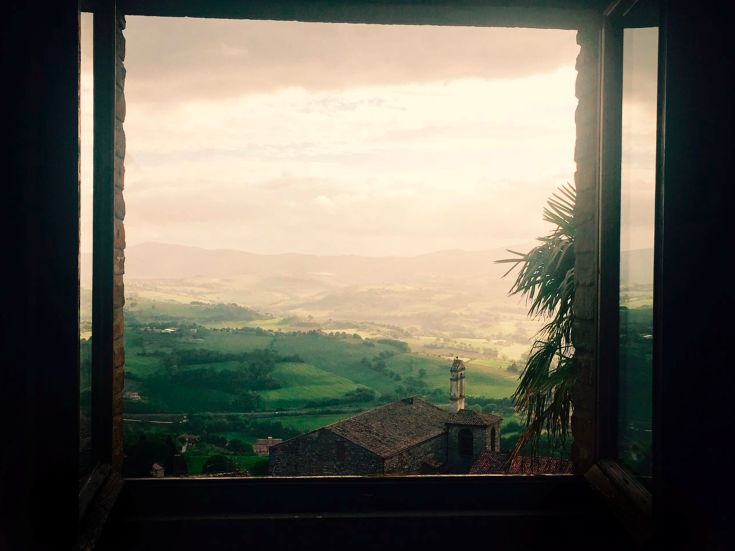 Un'apertura di finestra rivela un paesaggio caratterizzato da colline verdi e nuvole nel cielo.
